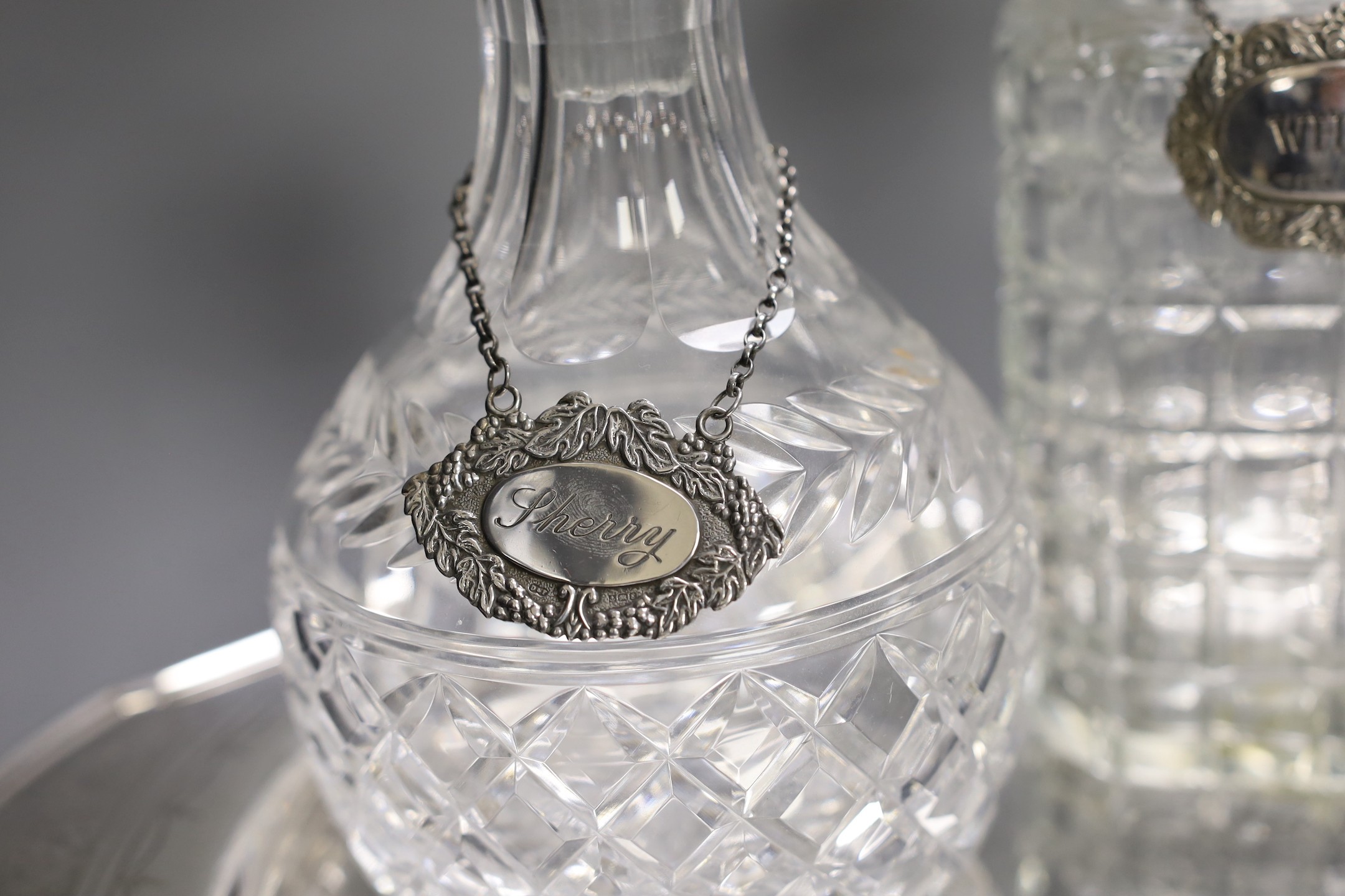A silver plated oval tray, five assorted cut glass decanters and five assorted silver wine labels.